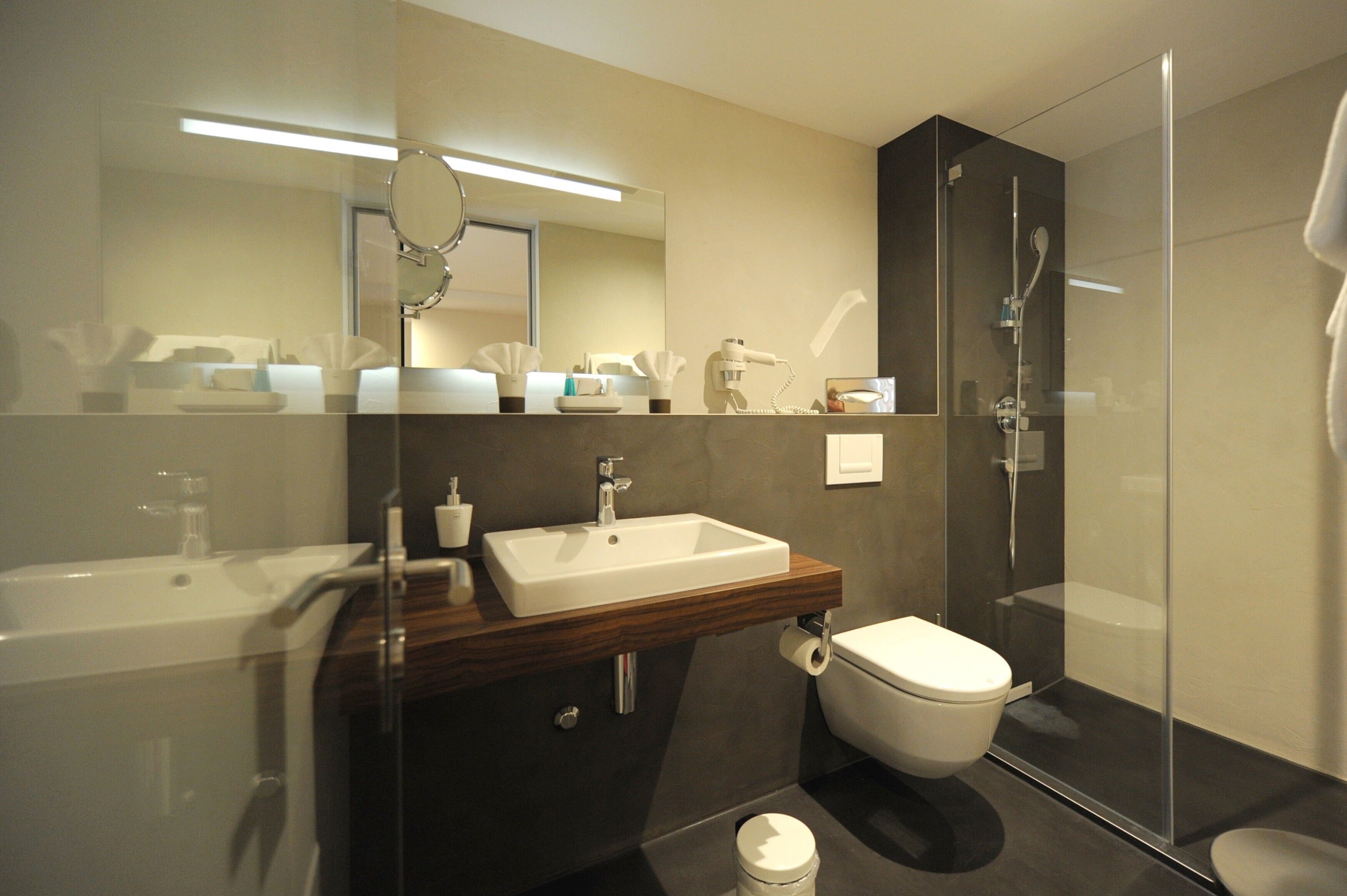 A modern bathroom with a glass shower enclosure, a wooden vanity, a white sink, and a toilet.