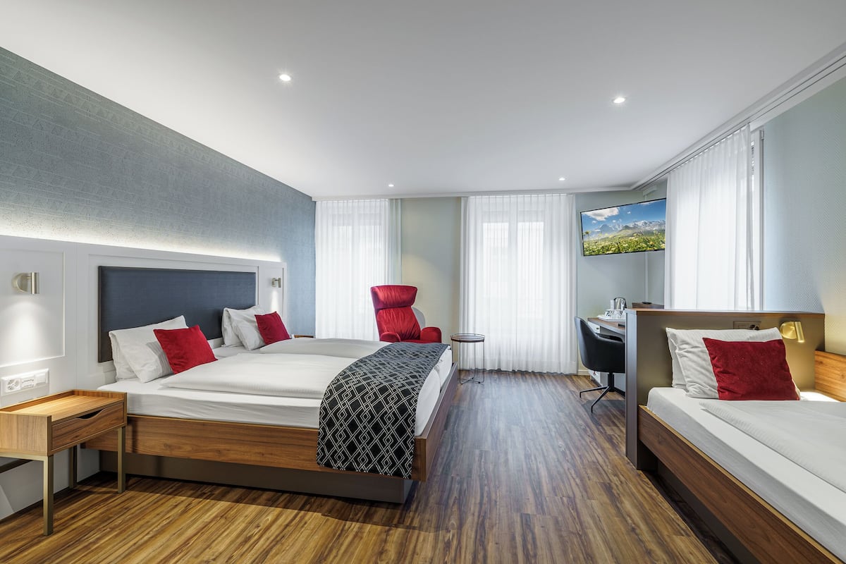 A modern hotel room with a large bed, a desk, and a view of a landscape.