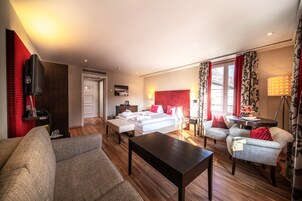 Una habitación de hotel con cama, sofá, mesa de centro, televisor y escritorio con lámpara.