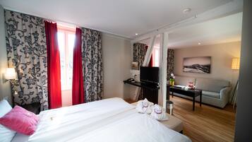Ett hotellrum med två sängar, ett skrivbord med en tv, en soffa och en tavla på väggen.