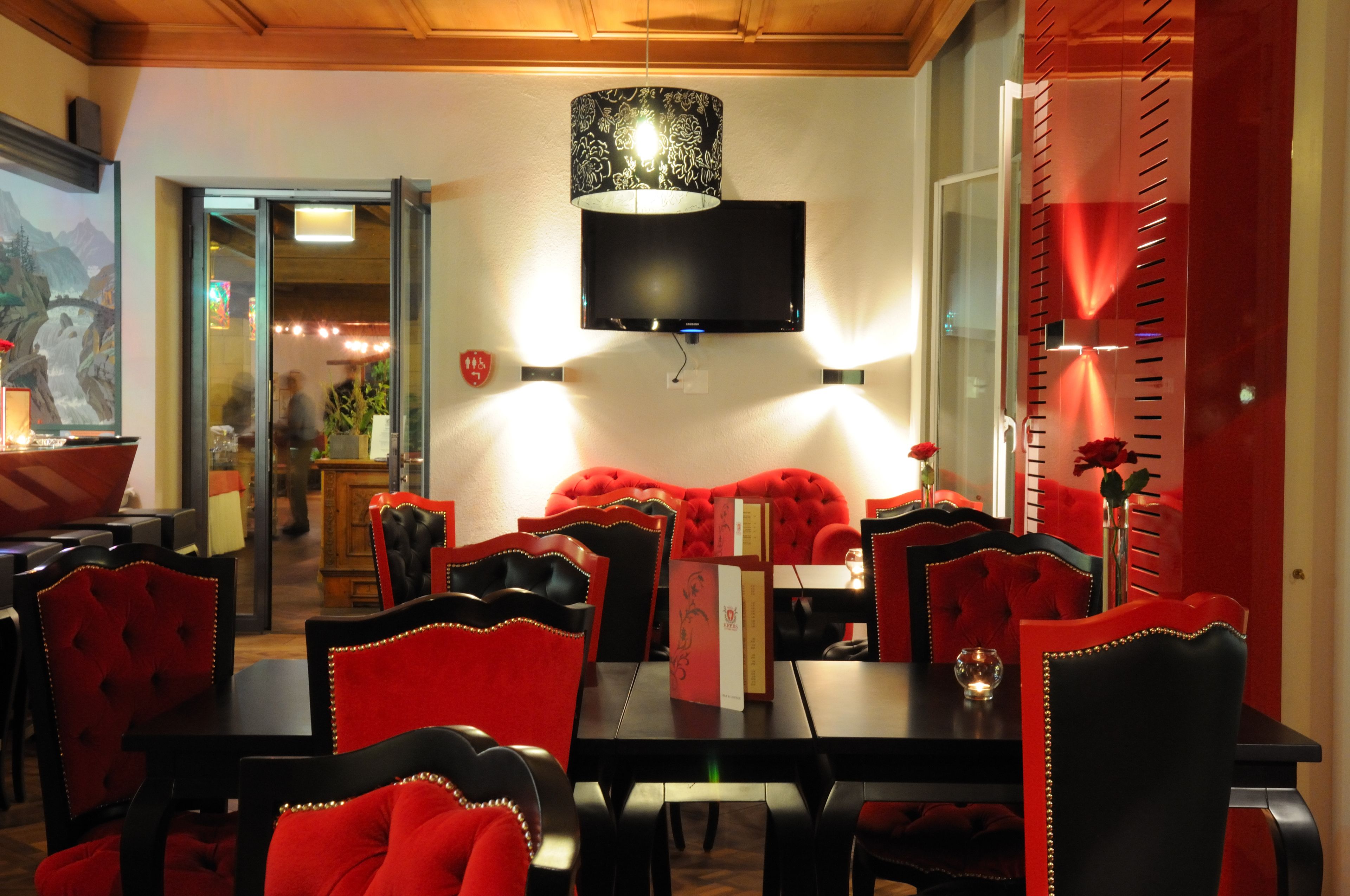 Un comedor con sillas tapizadas rojas, una mesa negra y un televisor de pantalla plana montado en la pared.