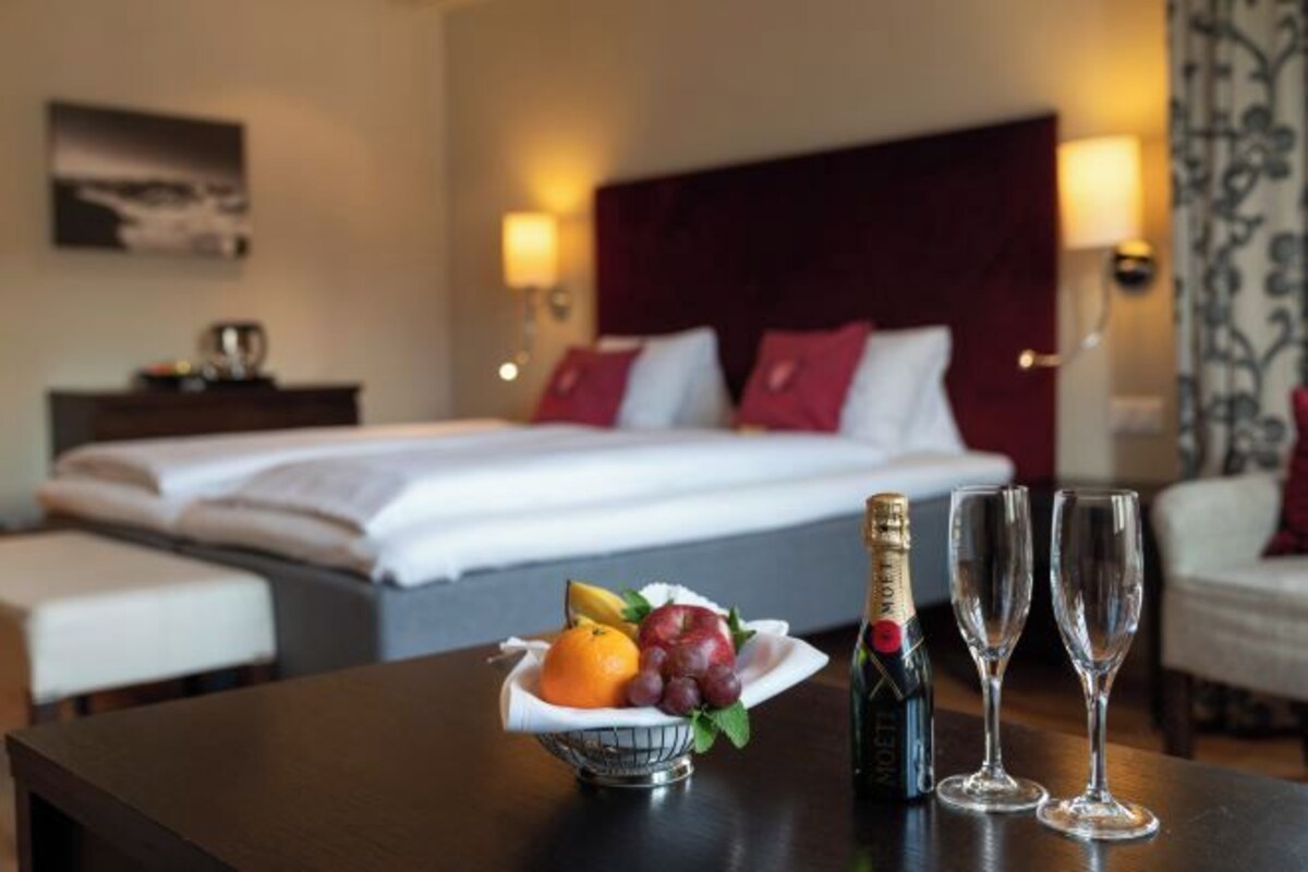 Ett hotellrum med en snyggt bäddad säng, ett nattduksbord med en fruktskål, två flaskor champagne och två tomma glas.