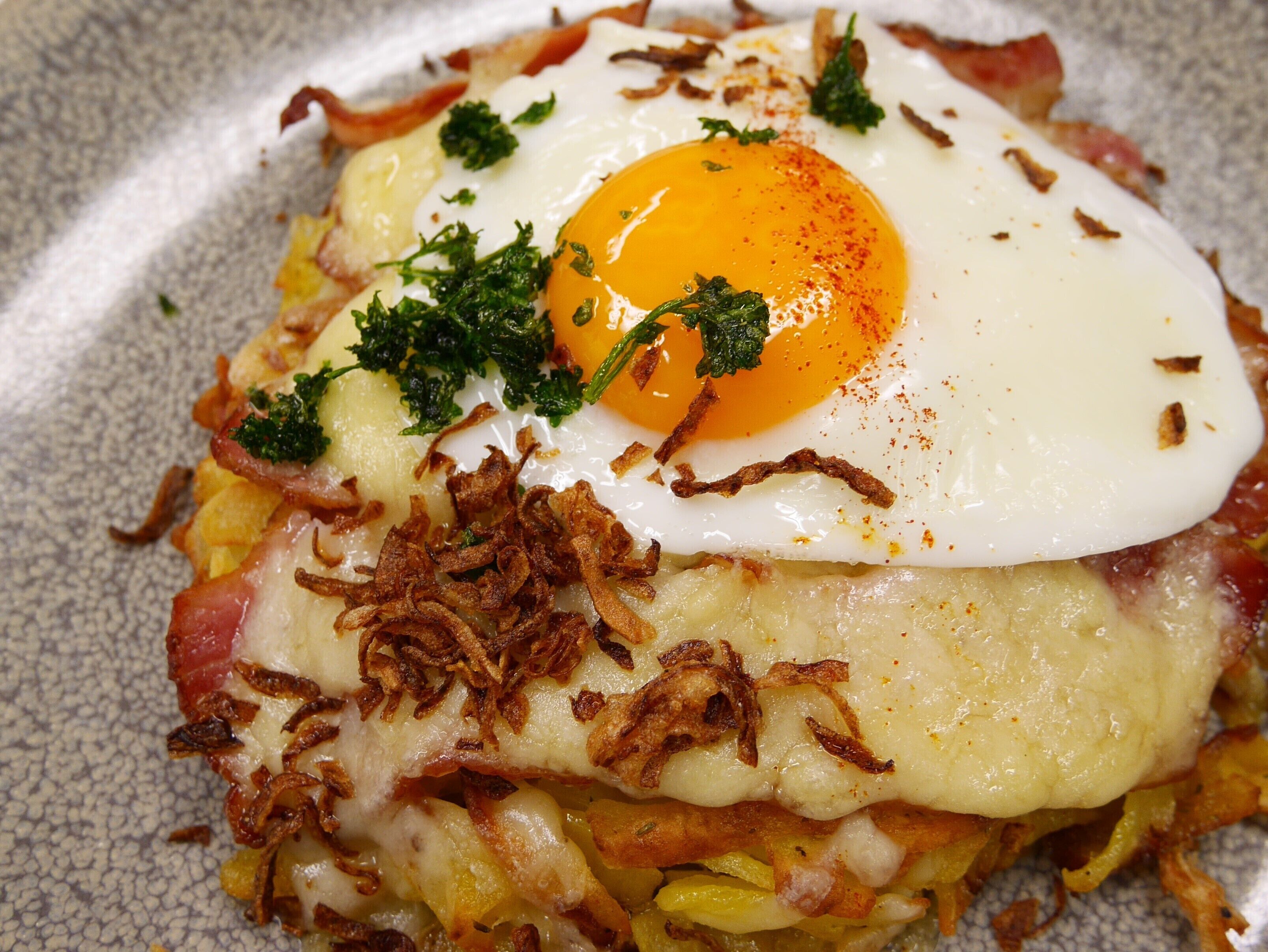 Un plat pour le petit-déjeuner composé d’un œuf frit, de fromage et de lardons croustillants.