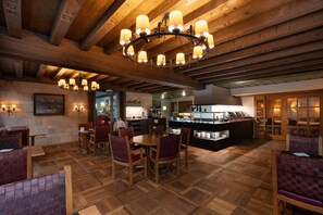 A restaurant with wooden floors, a central dining area with tables and chairs, a bar area with a counter, and a chandelier. - Hotel Krebs (Interlaken)