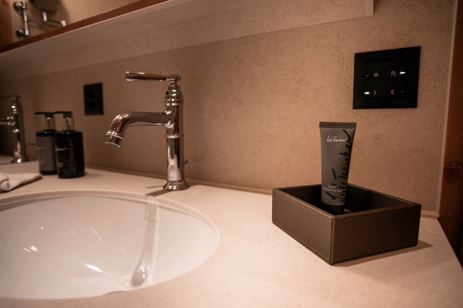A bathroom with a large sink, a modern faucet, and a hair conditioner tube in a box.