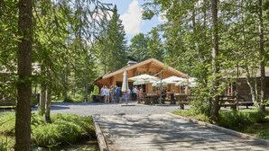 Une terrasse en bois mène à un bâtiment rustique doté d’un espace extérieur avec des sièges et des parasols.
