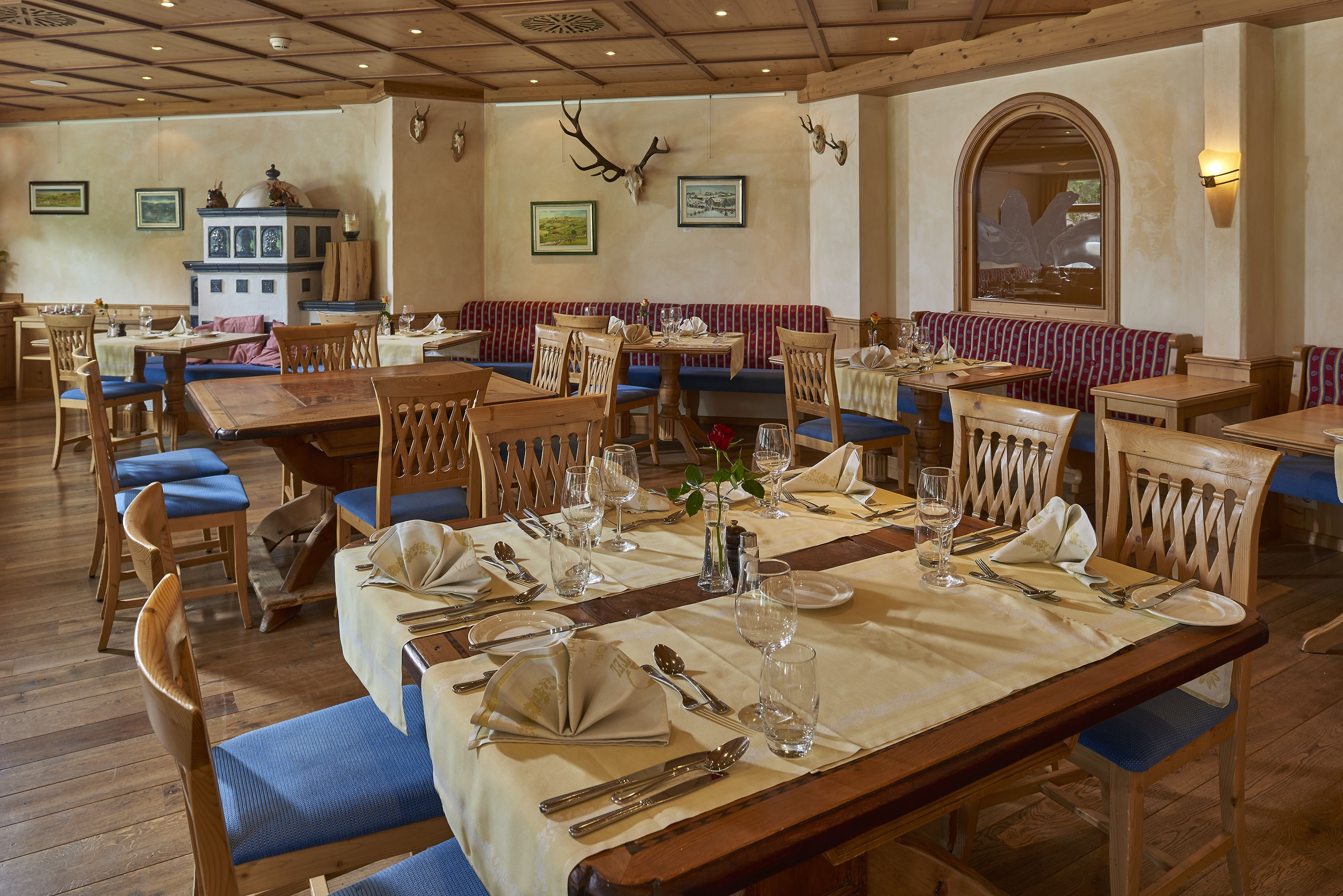 Un restaurante con mobiliario de madera, una mesa central para comer dispuesta con platos, vasos y cubiertos, y un banco con estampado rojo y azul.