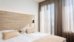 A modern hotel room with a wooden headboard, two beds with beige bedding, and sheer curtains allowing natural light. - Hotel DU LAC Locarno (Locarno)