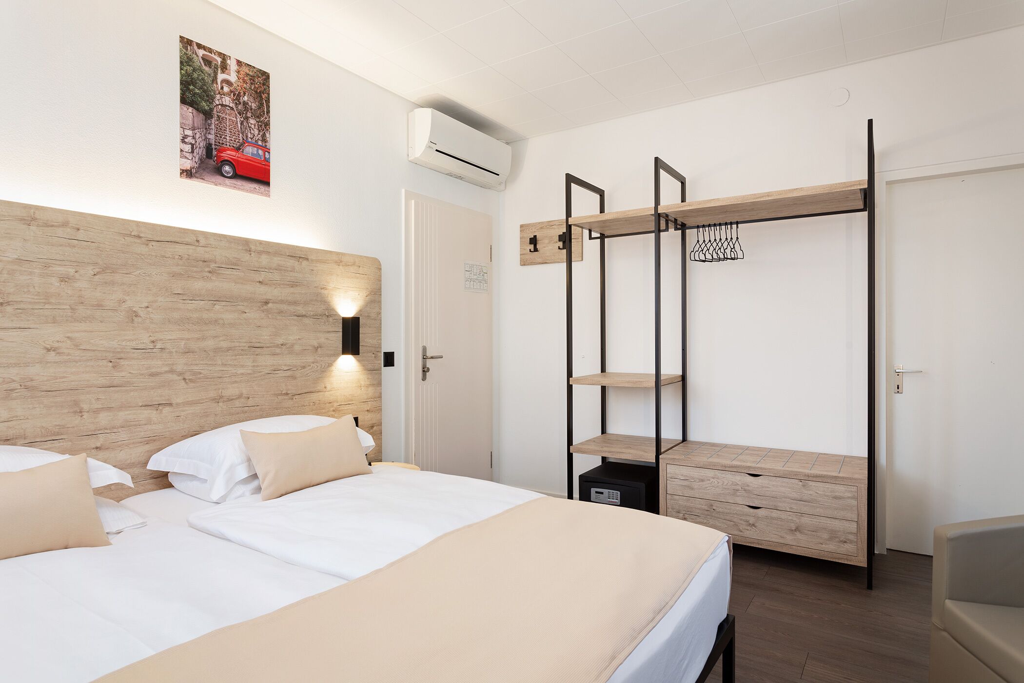 Um quarto moderno com cabeceira de madeira, cama com roupa de cama branca, ar-condicionado fixado na parede e estante embutida de madeira.