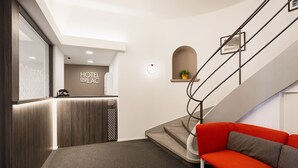 A hotel reception area with a wooden reception desk, a red sofa, and a staircase. - Hotel DU LAC Locarno (Locarno)