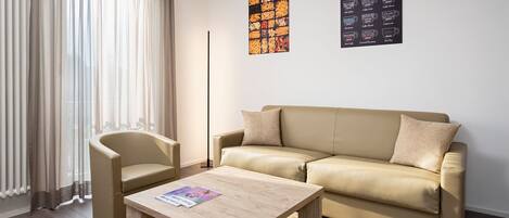 Uma sala de estar moderna com um sofá bege, uma mesa de centro de madeira e um abajur.
