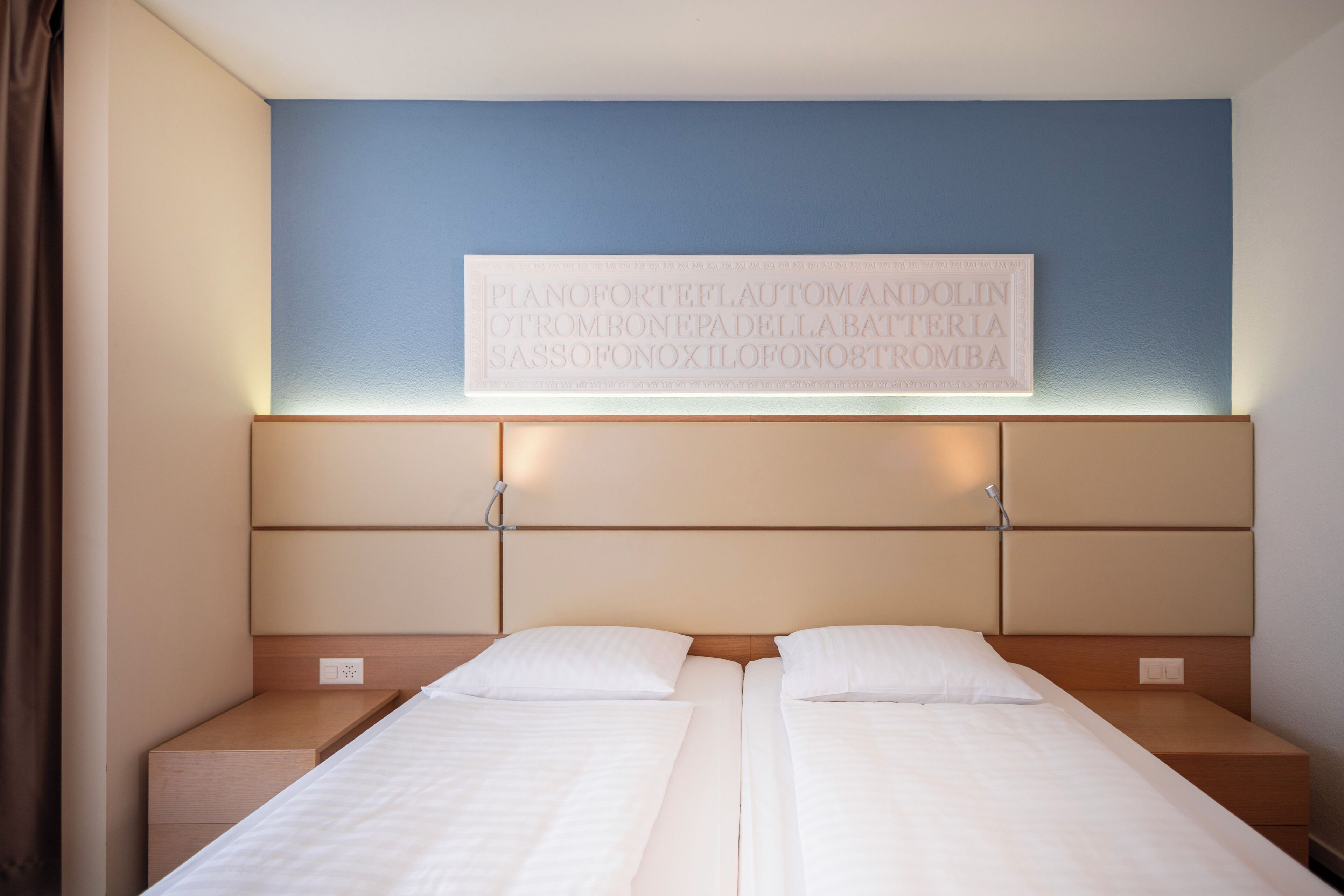 A hotel room with two beds, a blue accent wall, and a framed text above the beds.