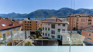 Vista desde un balcón con vistas a un paisaje urbano que incluye edificios, una masa de agua y montañas al fondo.