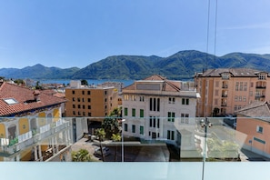 Vista desde un balcón con vistas a un paisaje urbano que incluye edificios, una masa de agua y montañas al fondo.