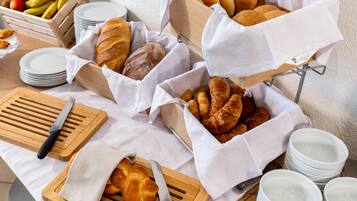 A breakfast buffet with bread, pastries, and fruits.