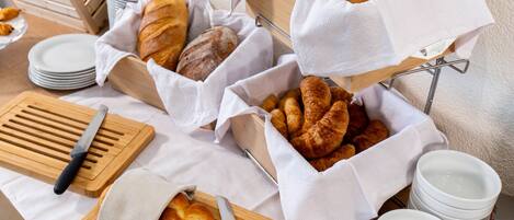 A breakfast buffet with bread, pastries, and fruits.