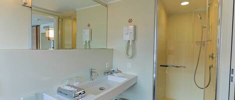 A modern bathroom with a large mirror, two sinks, a shower, and a toilet.