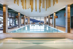 Ein moderner, überdachter Pool mit Glaswänden, Holzbalken und Sitzbereichen.