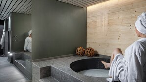 A spa area with a stone bathtub, wooden wall, and a reflection of a person in a robe.