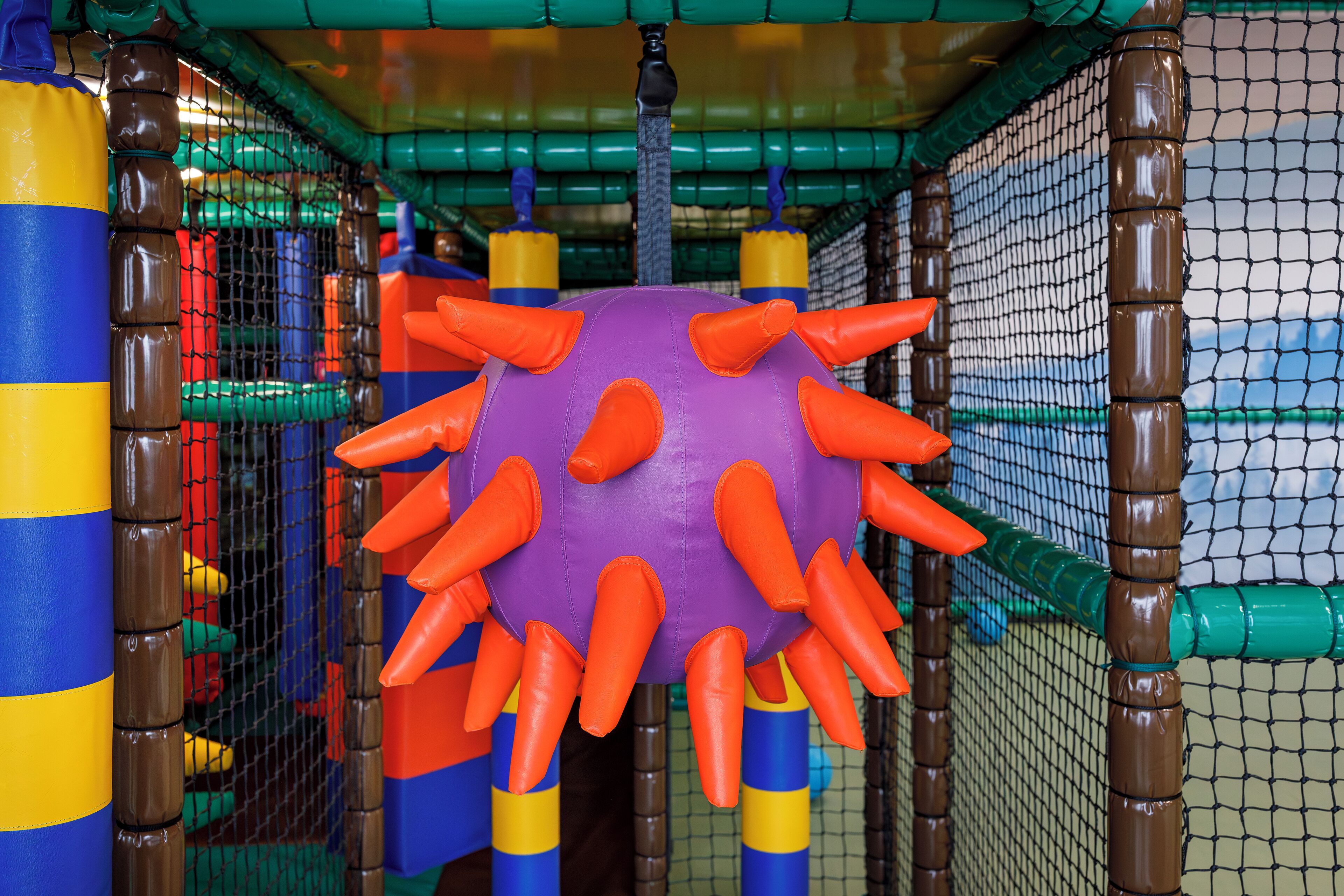 A play structure with a purple ball and orange spikes, surrounded by netting and colorful barriers.
