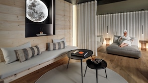 A modern living room with a large moon mural, a grey sofa, a black coffee table, and a person reading a book.