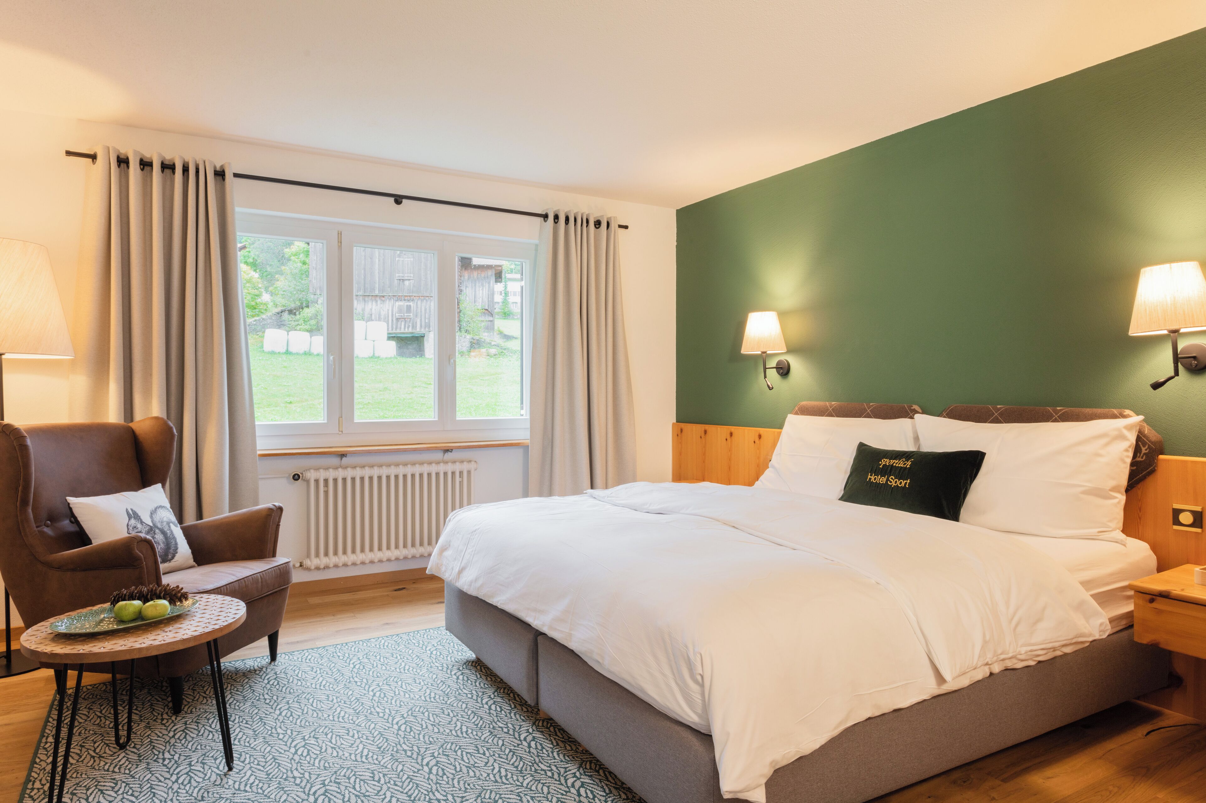 Une chambre à coucher comprenant un lit, une chaise, une petite table, une fenêtre avec des rideaux et une lampe fixée au mur.