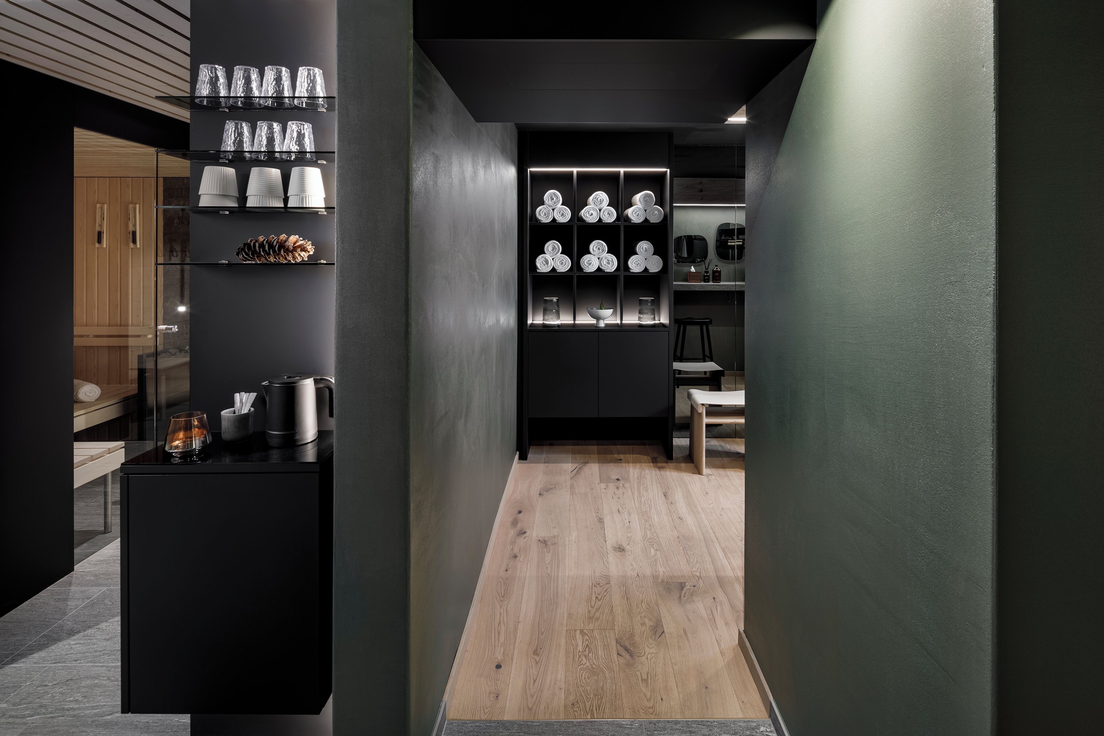 A modern kitchen with black cabinetry, a wooden floor, and glass shelves displaying kitchenware.