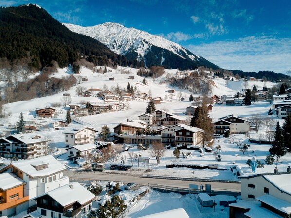 A snow-covered village with buildings, a road, and a mountain in the background.