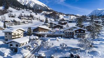Uma aldeia montanhosa coberta de neve, com edifícios em estilo chalé, uma estância de esqui e um hotel chamado "Hotel Sport".