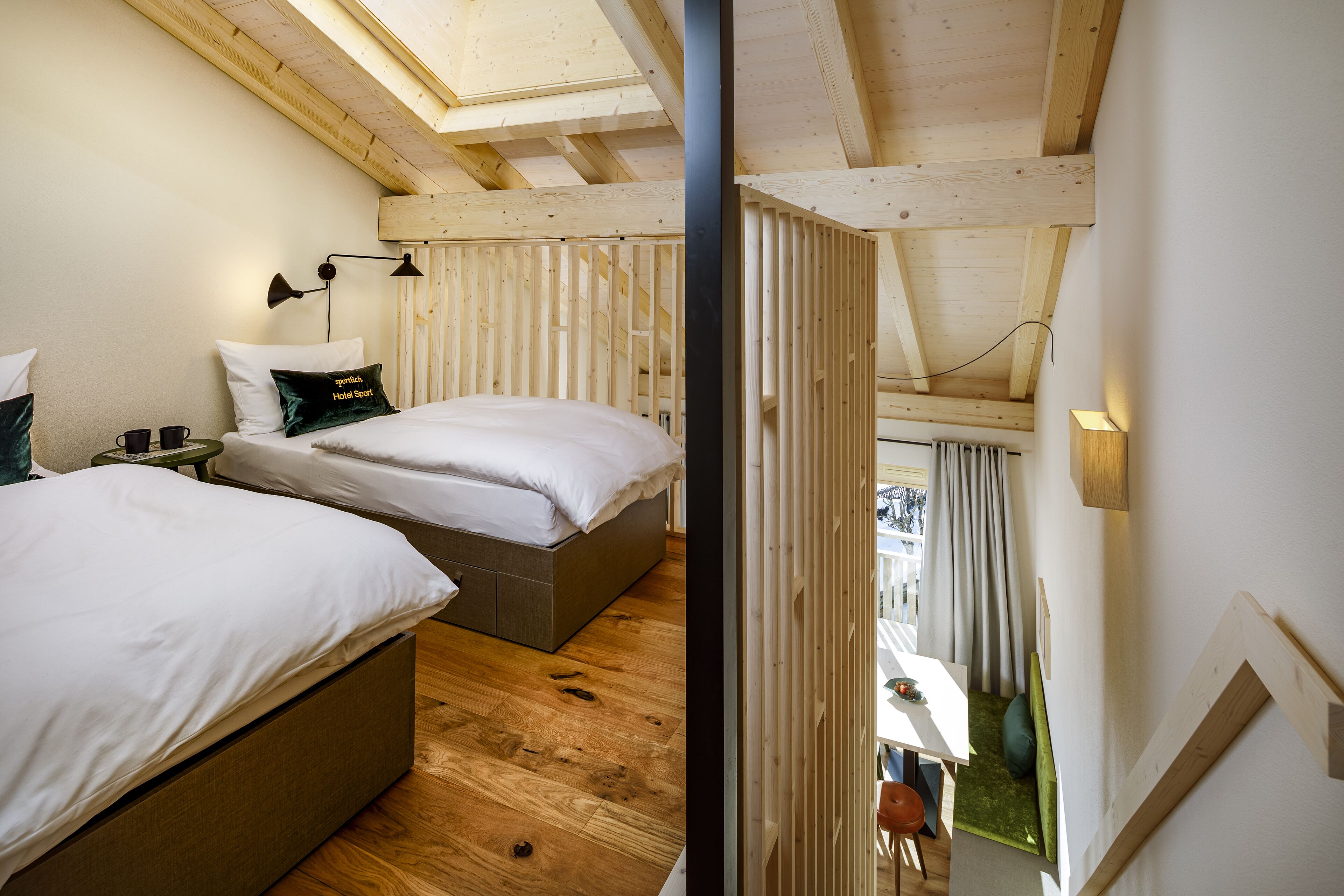 A bedroom with two beds, wooden flooring, a skylight, and a view of the outdoors.