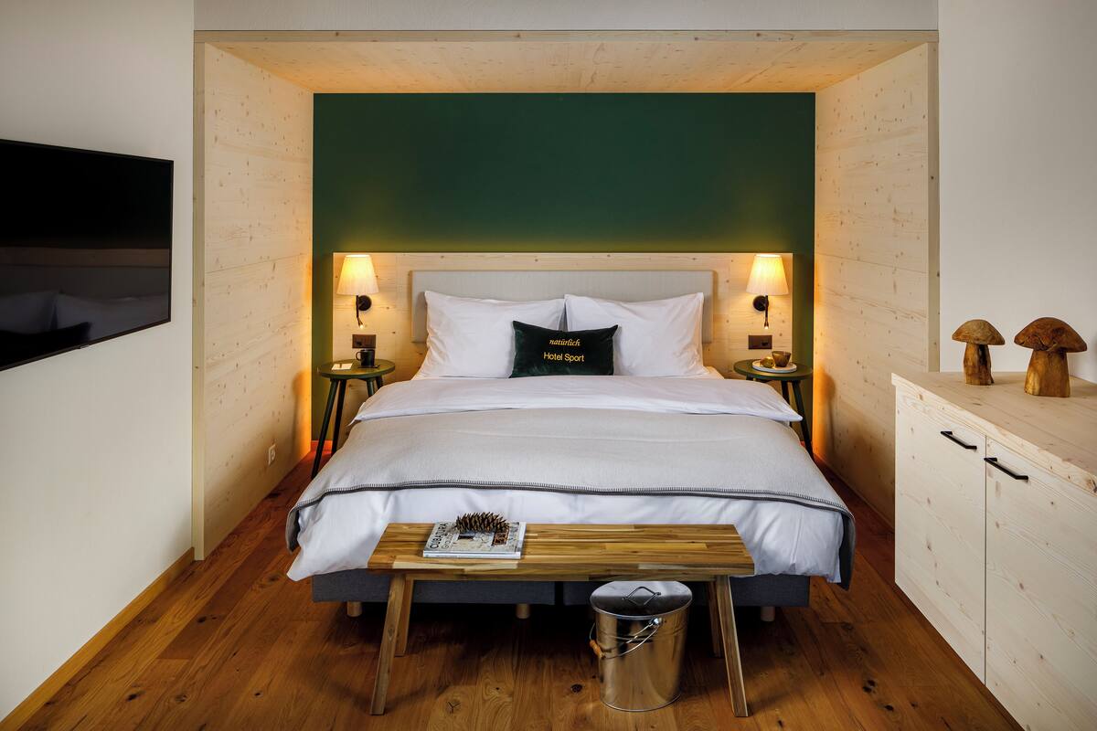 A neatly arranged bedroom with a bed, bedside tables, a small wooden table, and a trash bin.