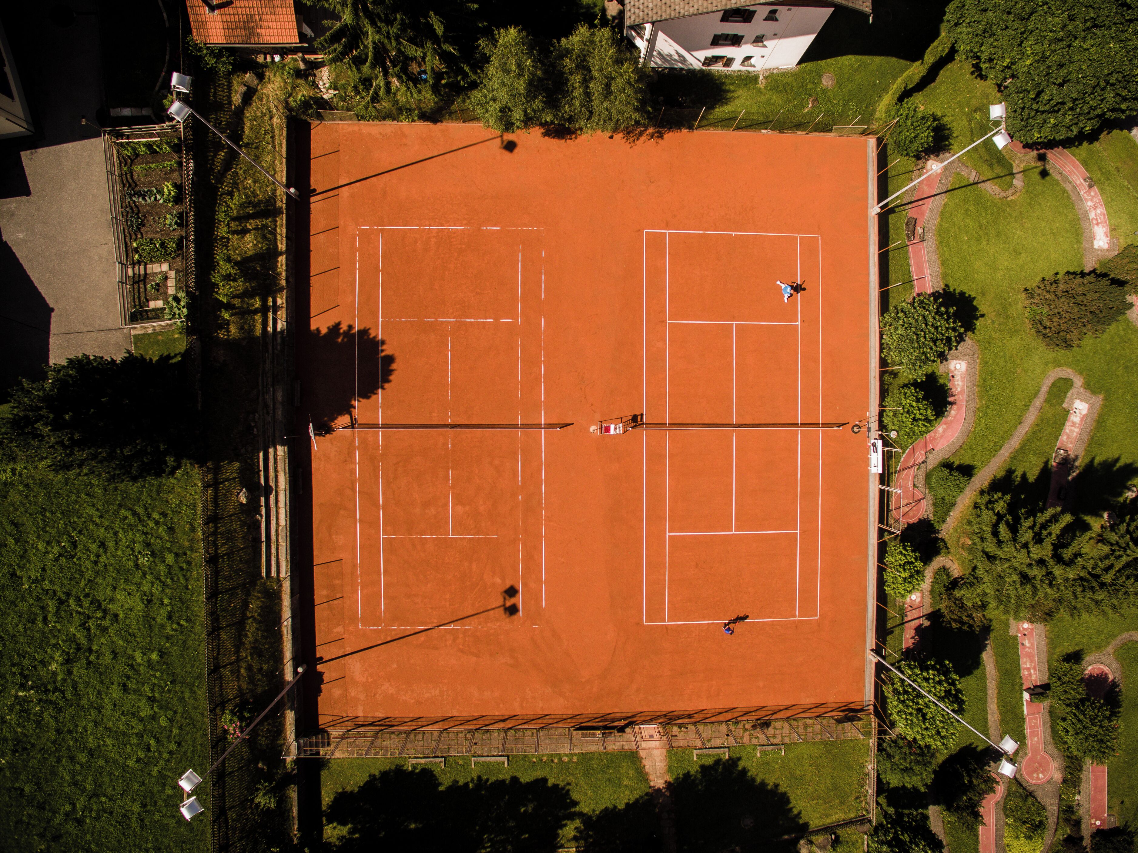 Vista aérea de una cancha de tenis rodeada de vegetación y edificios.