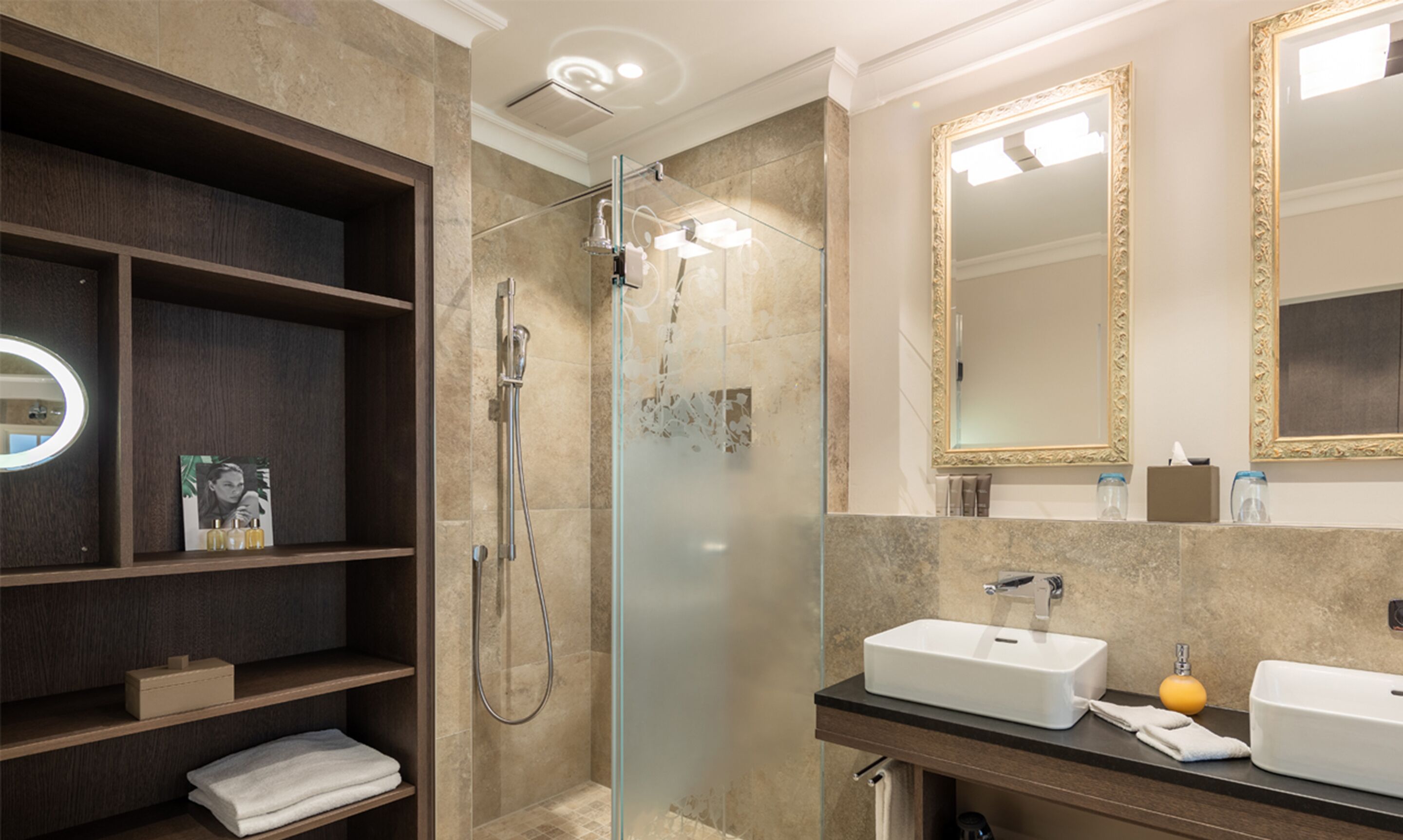 A modern bathroom with a glass-enclosed shower, a vanity with two sinks, and a large mirror with an ornate frame.