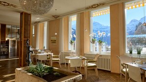 Un comedor con mesas dispuestas para dos, ventanas amplias con vistas a la montaña y una lámpara decorativa.