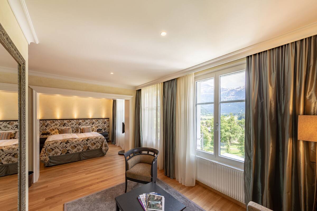 Una habitación de hotel con una cama grande, una cama más pequeña, una silla, una mesa y vistas al exterior.