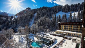Paisaje nevado con área de piscina, rodeado de árboles y un edificio con amplias ventanas.