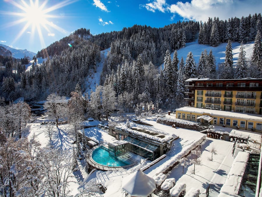 A snow-covered landscape with a pool area, surrounded by trees and a building with multiple windows.