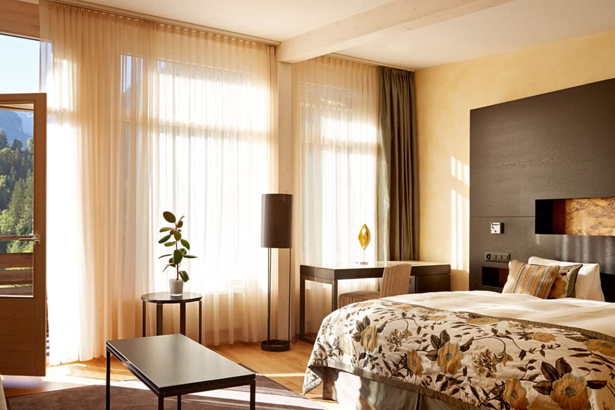 Habitación de hotel con cama, escritorio, silla, lámpara y vistas al exterior.