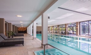A modern indoor swimming pool with lounge areas and large windows.