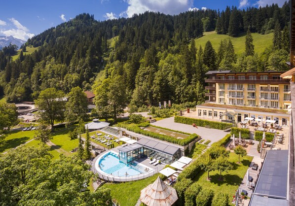 A hotel with a swimming pool, outdoor seating, and a view of a forested mountain.