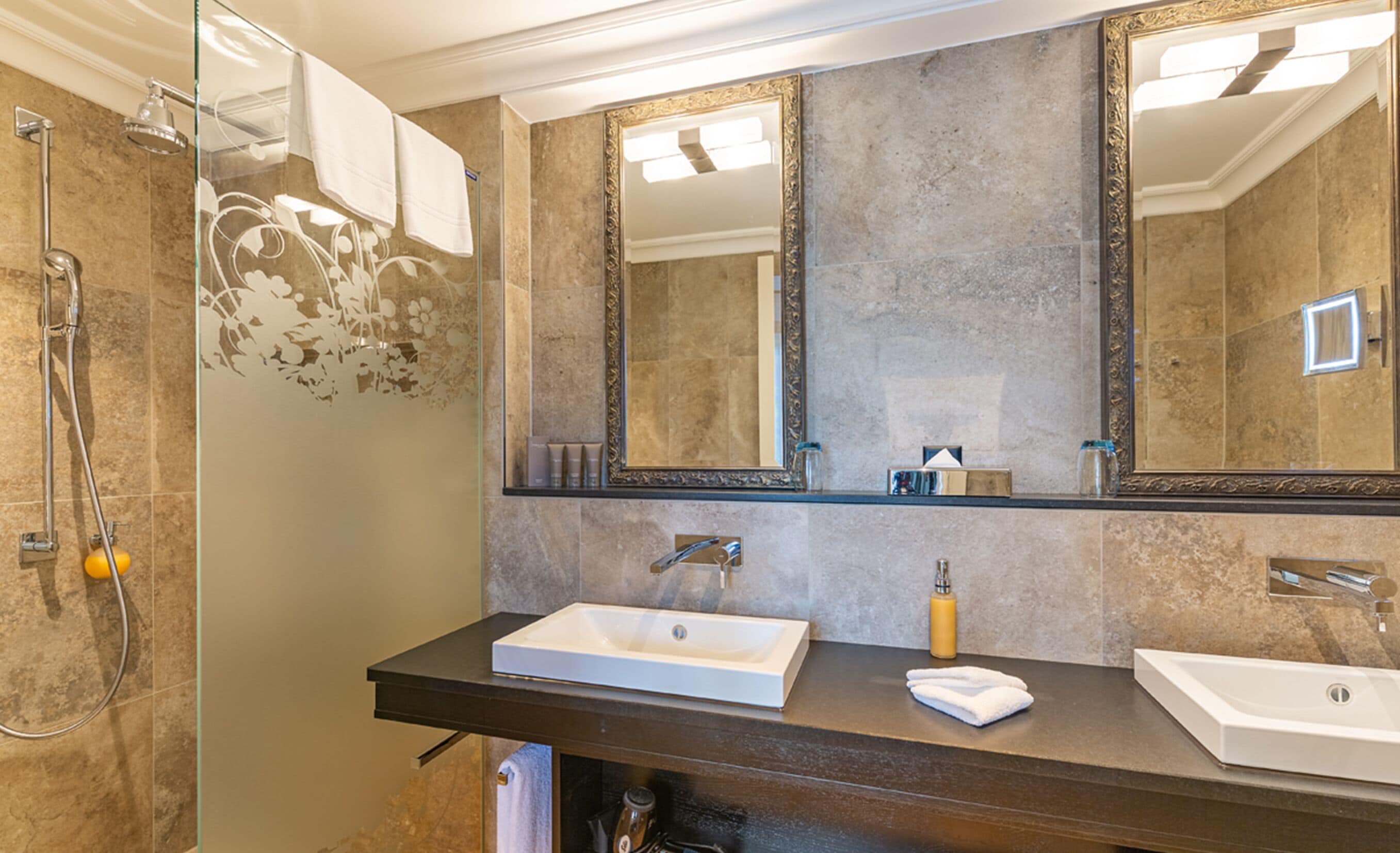 Une salle de bain avec un grand miroir, deux lavabos et une douche.