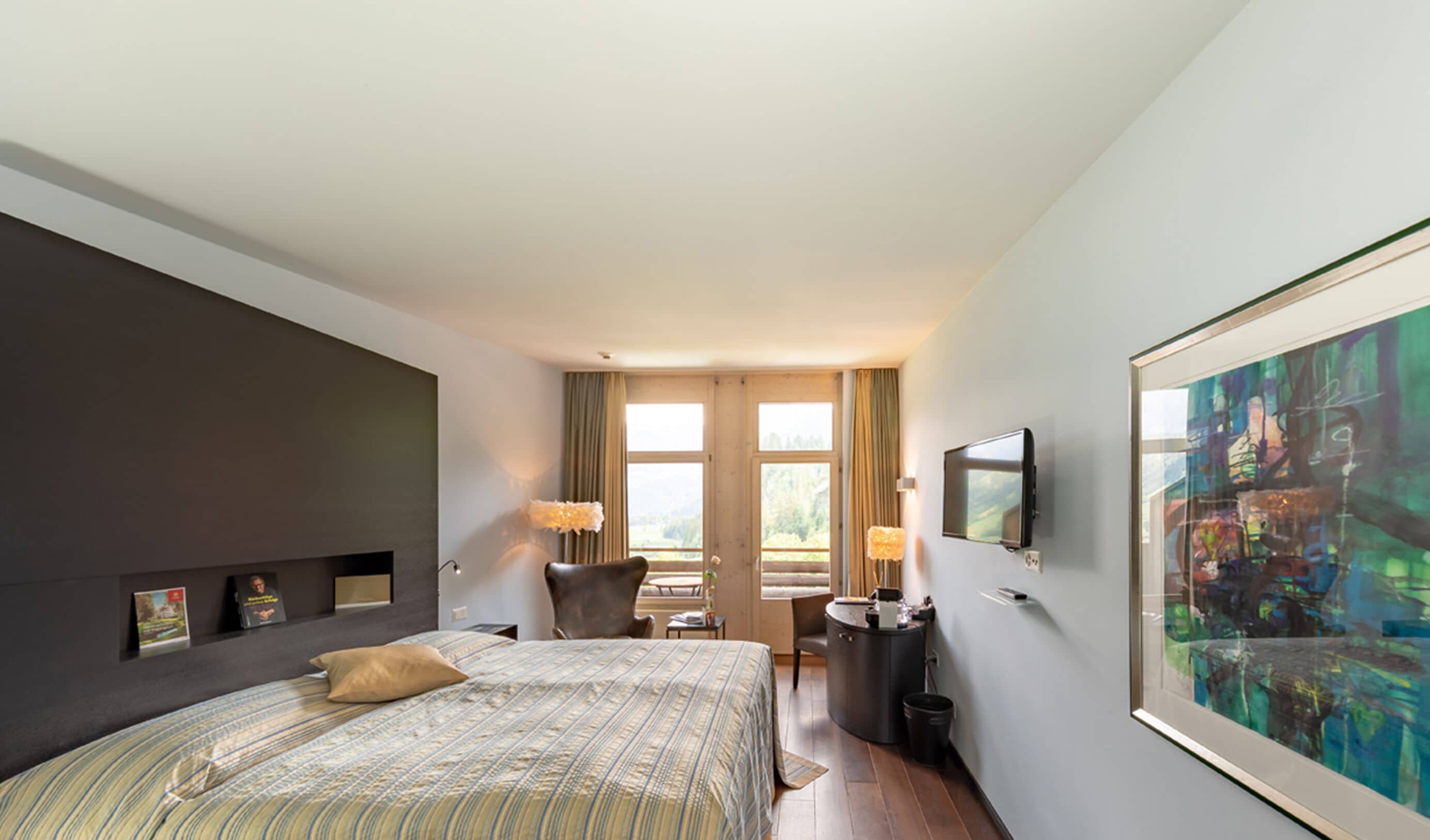 A hotel room with a bed, a desk, a chair, a TV, and a painting on the wall.