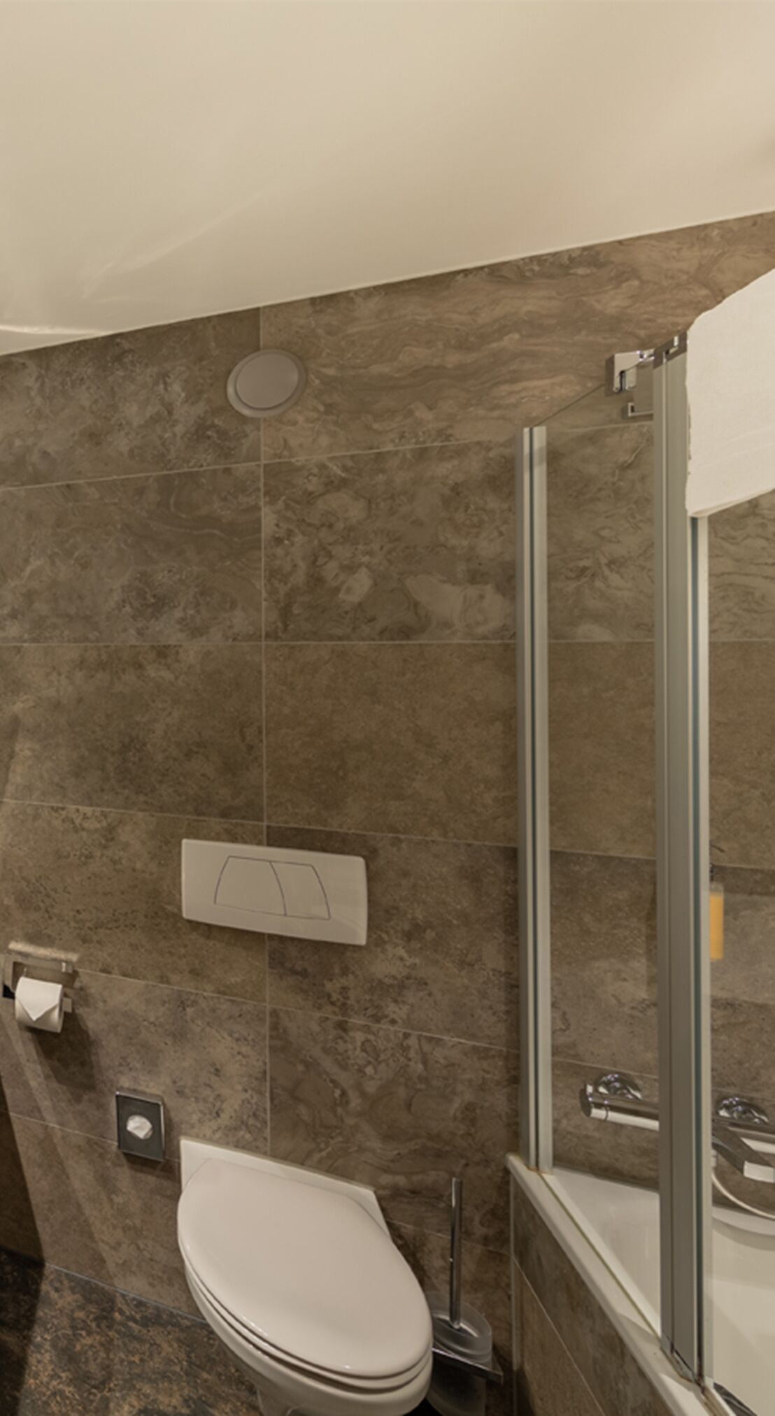 A bathroom with a toilet, a shower, and a wall-mounted toilet paper holder.