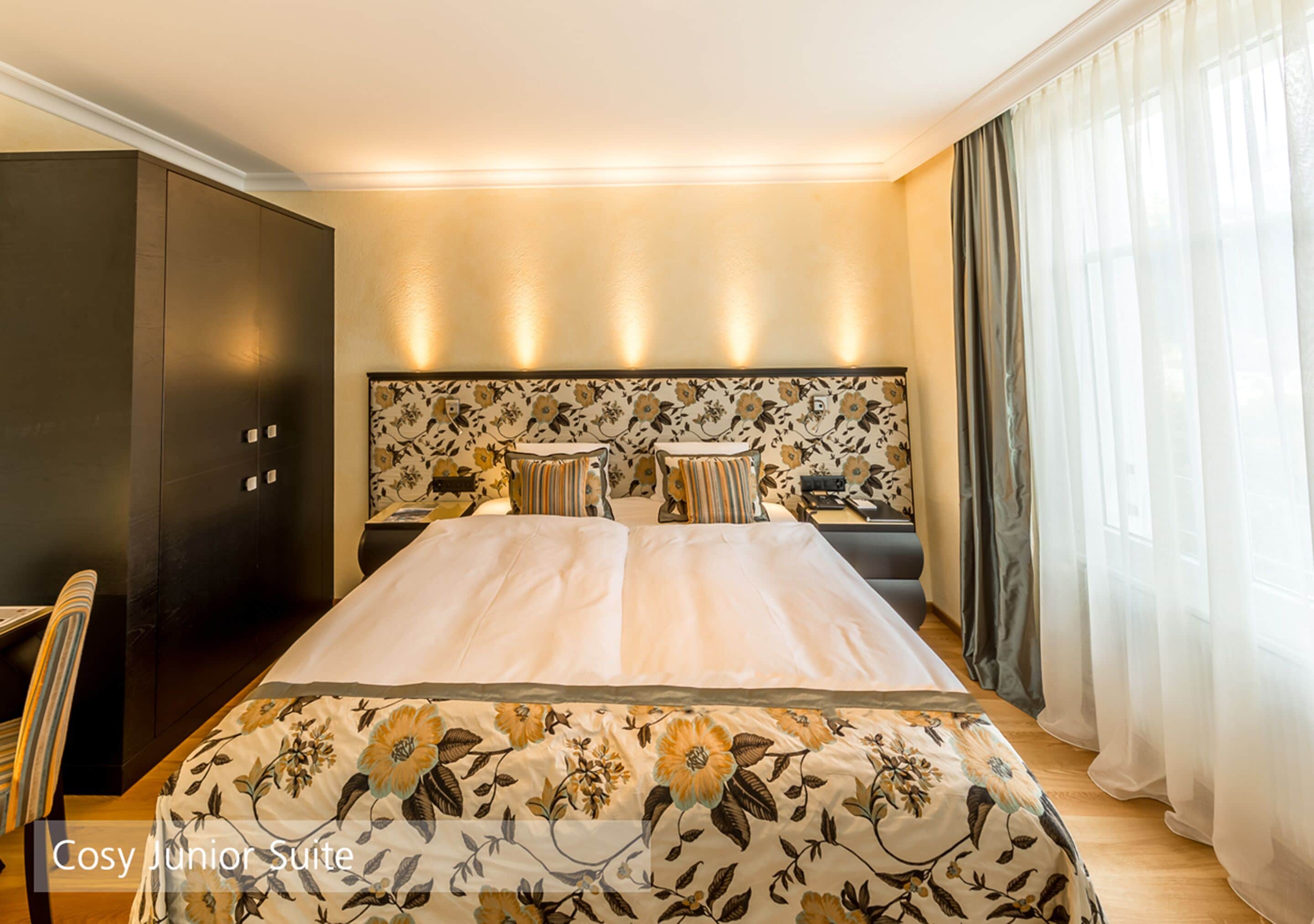 A bedroom with a large bed, a headboard with a floral pattern, a bedside table, and a wardrobe.