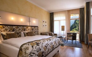 A hotel room with a large bed, a sofa, a desk, and a view of the outdoors.