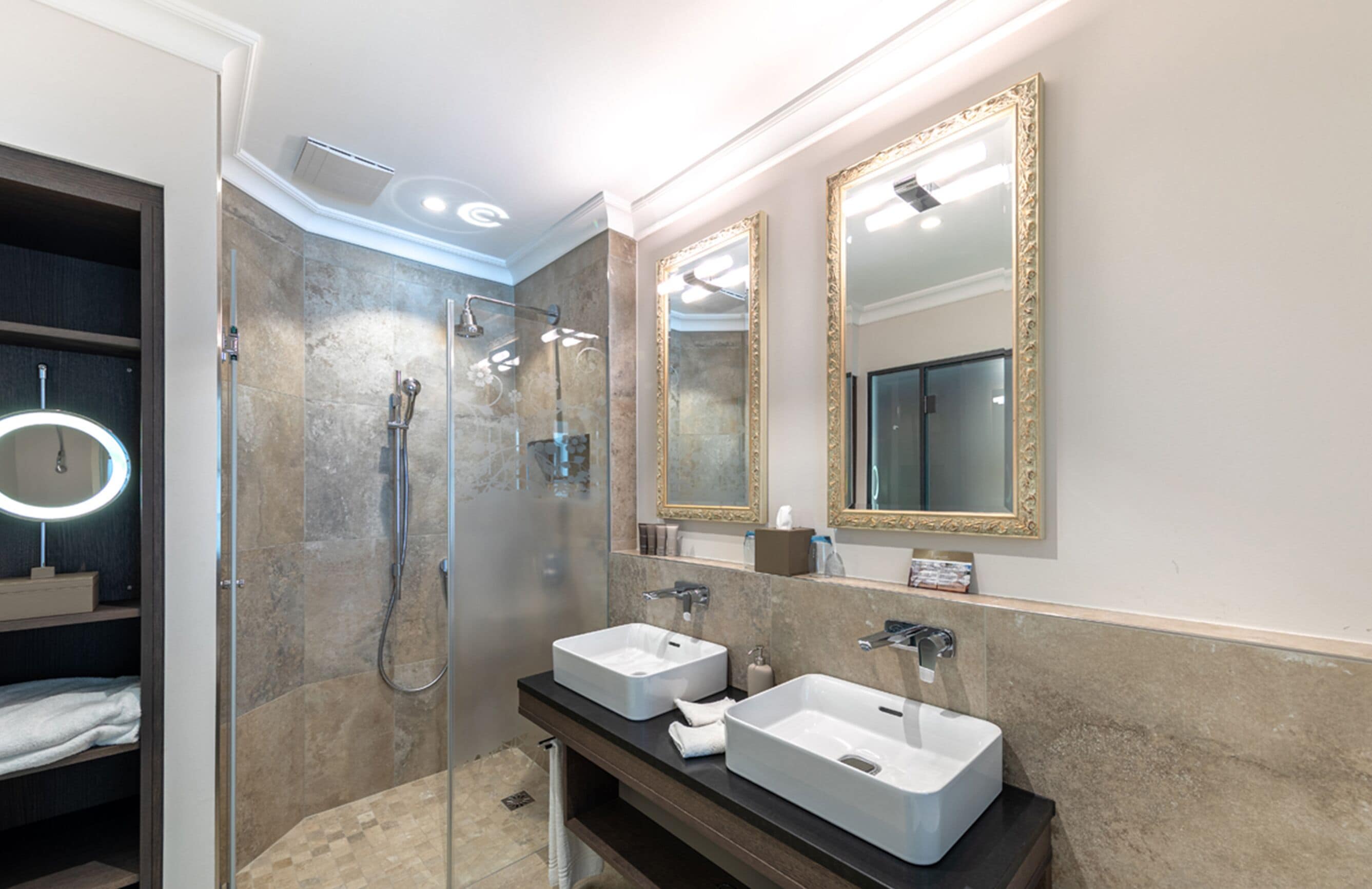A modern bathroom with two sinks, a walk-in shower, and a large mirror with a gold frame.