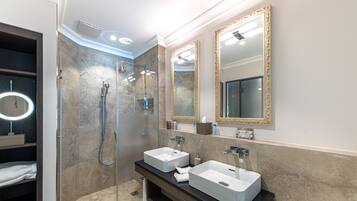A modern bathroom with two sinks, a walk-in shower, and a large mirror with a gold frame.