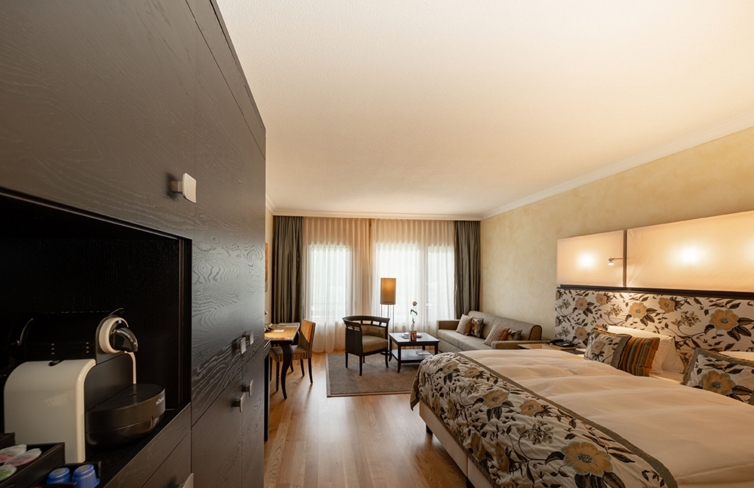 A hotel room with a bed, a desk, a chair, a sofa, and a coffee machine.
