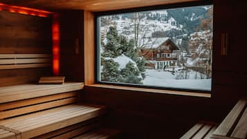 Una sauna con bancos de madera y una ventana que ofrece vistas a un paisaje montañoso nevado.