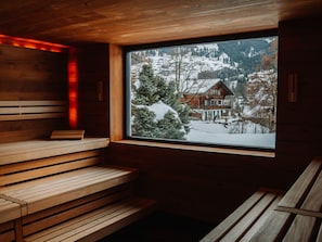 A sauna with wooden benches and a window offering a view of a snowy mountain landscape. - Lenkerhof Gourmet Spa Resort (Lenk)